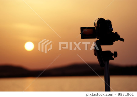 Silhouette of a camera taking videos of a sunset 9851901