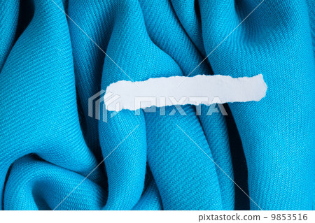 Blank scrap of paper on blue cloth wavy folds textile background Blank scrap of paper on blue cloth wavy folds textile background 9853516
