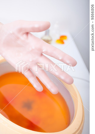 Female hand orange parrafin wax in bowl. Manicure beauty spa salon 9866806