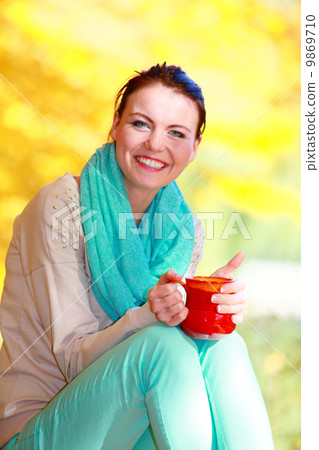 Happy girl relaxing in the autumn park enjoying hot drink Happy girl relaxing in the autumn park enjoying hot drink 9869710