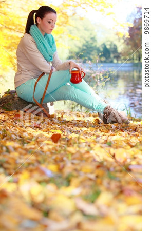 Girl relaxing in the autumn park enjoying hot drink 9869714