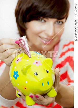 Young woman gives money to decorative ceramic piggy bank Young woman gives money to decorative ceramic piggy bank 9878242