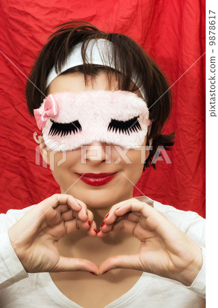 Attractive woman in sleep mask making heart shape with her hands Attractive woman in sleep mask making heart shape with her hands 9878617
