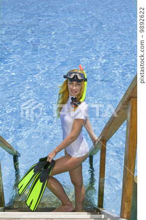 Sports woman stands with equipment for Snorkeling on steps of villa on piles on water. .Maldives... 9892622