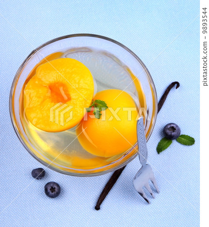 Peach compote in glass bowl with fork, blueberries and vanilla 9893544