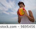 Asian young good looking man with a colourful ball on the beach eyes closed 9895456
