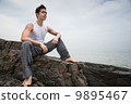 Asian man sitting on rocks looking out and smiling 9895467
