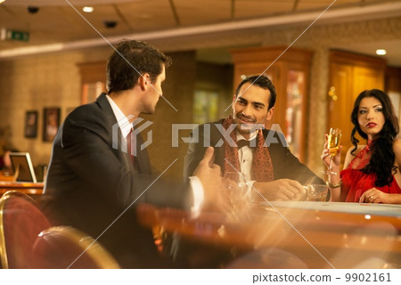 Happy young people behind gambling table with drinks 9902161