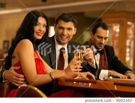 Happy young people behind gambling table with drinks Happy young people behind gambling table with drinks 9902163