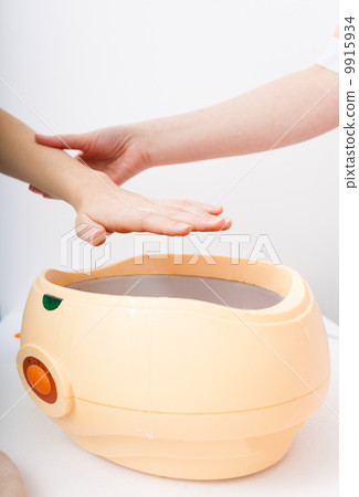 Female hand and orange paraffin wax bowl. Woman in beauty salon Female hand and orange paraffin wax bowl. Woman in beauty salon 9915934