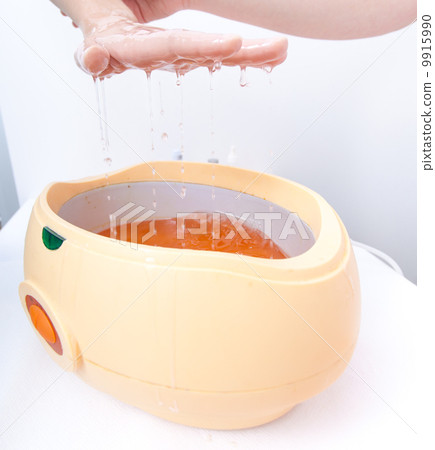 Female hand orange parrafin wax in bowl. Manicure beauty spa salon 9915990