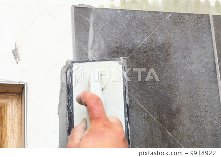 Construction worker is tiling at home, tile floor adhesive Construction worker is tiling at home, tile floor adhesive 9918922