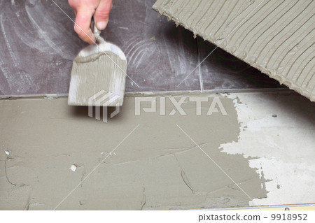 Construction worker is tiling at home tile floor adhesive 9918952