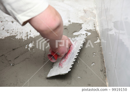 Construction worker is tiling at home tile floor adhesive 9919150