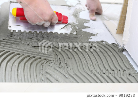 Construction worker is tiling at home, tile floor adhesive 9919258