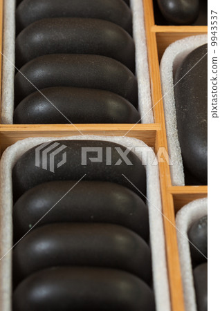 Black spa zen massage stones in wooden case as background 9943537