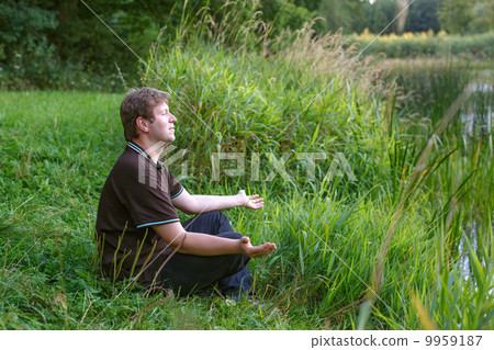 Young handsome man sitting near forest lake and relaxing Young handsome man sitting near forest lake and relaxing 9959187