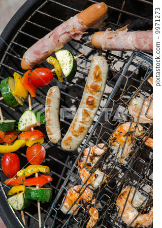 Sausages, big prawns and vegetable skewers smoking on grill 9971273