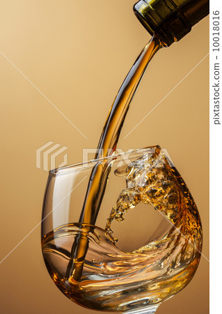 Cognac pouring from bottle into glass with splash on brown backg 10018016