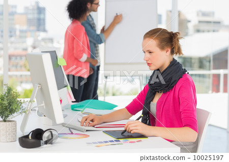 Female artist using graphic tablet with colleagues at office Female artist using graphic tablet with colleagues at office 10025197