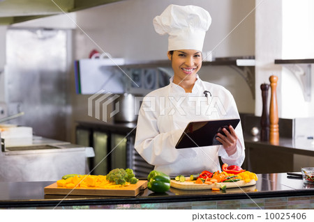 Smiling chef using digital tablet while cutting vegetables Smiling chef using digital tablet while cutting vegetables 10025406