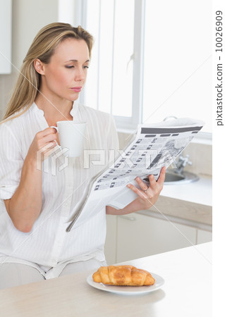 Serious woman holding mug and newspaper at breakfast Serious woman holding mug and newspaper at breakfast 10026909