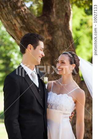 Happy newlywed couple standing in park 10027113