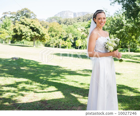 Happy bride holding flower bouquet in garden 10027246