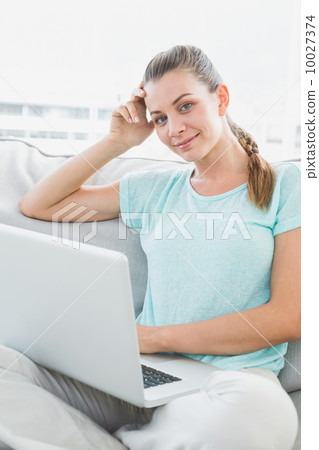 Smiling woman sitting on couch using her laptop 10027374