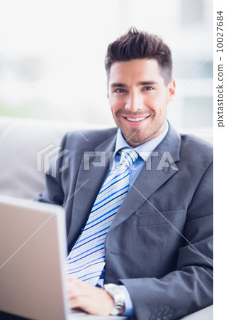 Happy businessman sitting on sofa using his laptop Happy businessman sitting on sofa using his laptop 10027684