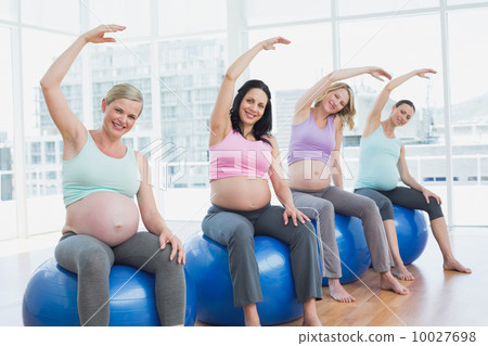 Pregnant women sitting on exercise balls stretching arms Pregnant women sitting on exercise balls stretching arms 10027698