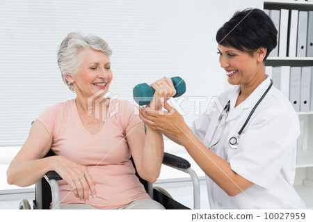 Physiotherapist assisting senior woman to lift dumbbell 10027959