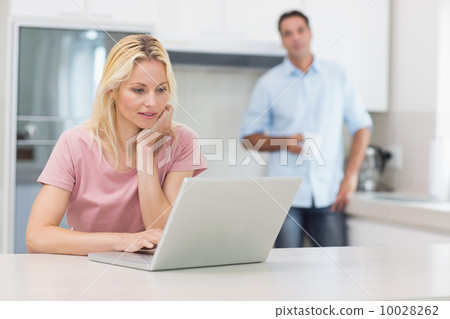 Woman using laptop with man drinking coffee in kitchen Woman using laptop with man drinking coffee in kitchen 10028262