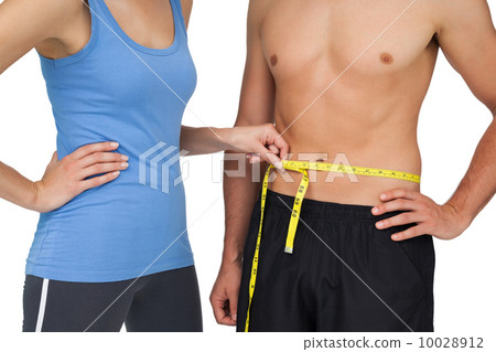 Mid section of a fit woman measuring mans waist 10028912