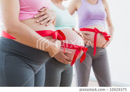 Pregnant women standing with red bow around bumps 10029375