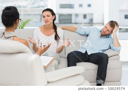 Angry couple sitting on couch talking to therapist 10029574