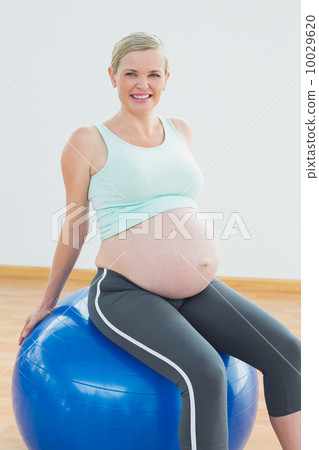 Happy blonde pregnant woman sitting on blue exercise ball Happy blonde pregnant woman sitting on blue exercise ball 10029620