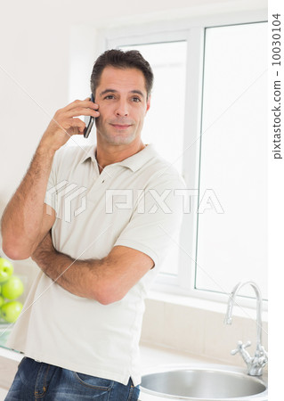Handsome man using mobile phone in kitchen Handsome man using mobile phone in kitchen 10030104