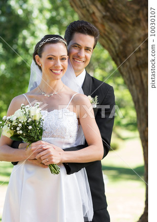 Happy groom embracing bride from behind in garden Happy groom embracing bride from behind in garden 10030107