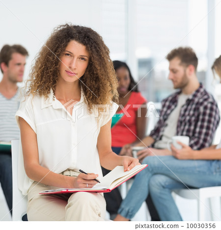Focused woman writing while colleagues are talking behind her 10030356