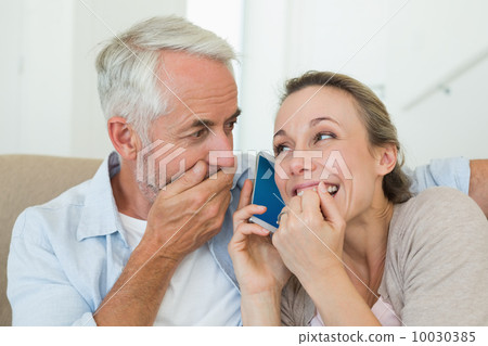 Happy couple listening to phone call together on the couch 10030385