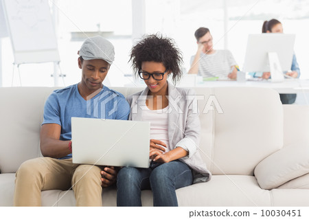 Couple using laptop with colleagues in background at creative of 10030451