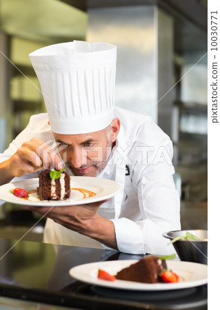 Concentrated male pastry chef decorating dessert in kitchen Concentrated male pastry chef decorating dessert in kitchen 10030771