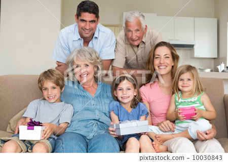 Siblings holding gifts with family in living room 10030843