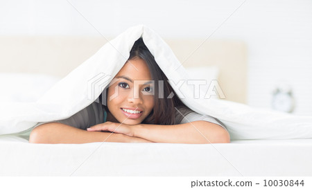 Pretty girl lying under the duvet smiling at camera 10030844
