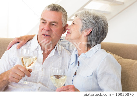 Senior couple sitting on couch drinking white wine Senior couple sitting on couch drinking white wine 10030870