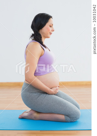 Happy pregnant brunette kneeling on exercise mat 10031042