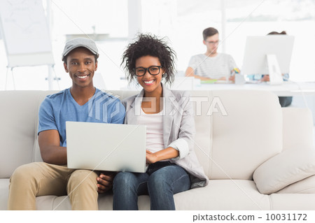 Couple using laptop with colleagues in background at creative of Couple using laptop with colleagues in background at creative of 10031172