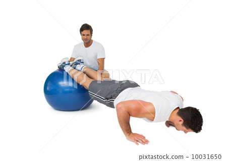 Male trainer helping young man exercise on fitness ball Male trainer helping young man exercise on fitness ball 10031650