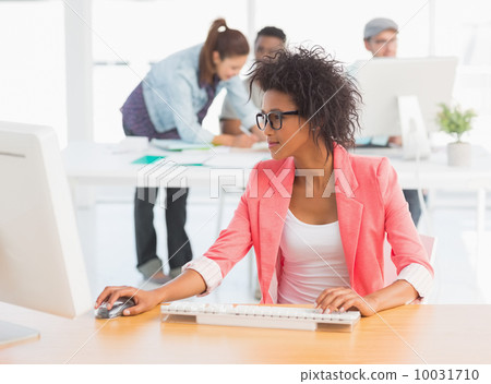 Female artist using computer with colleagues in background at of 10031710